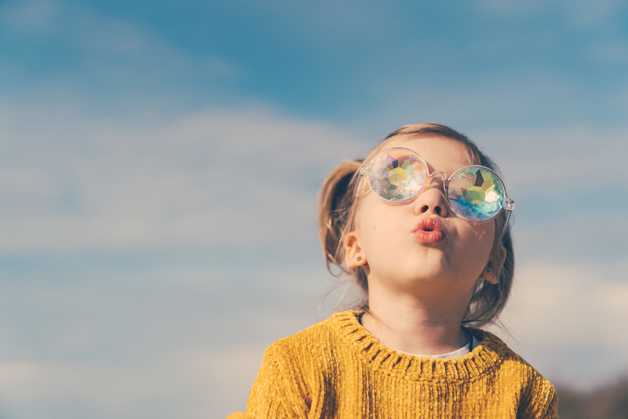little girl in funny kaleidoscope glasses is looking to the sky with open mouth and curiosity.